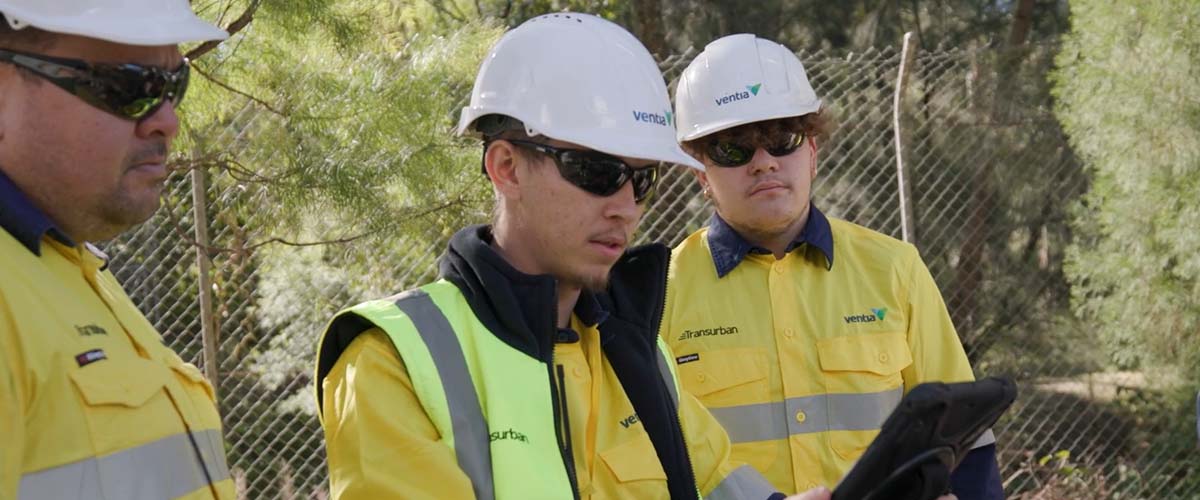 Three workers stand outside in high-vis clothing.